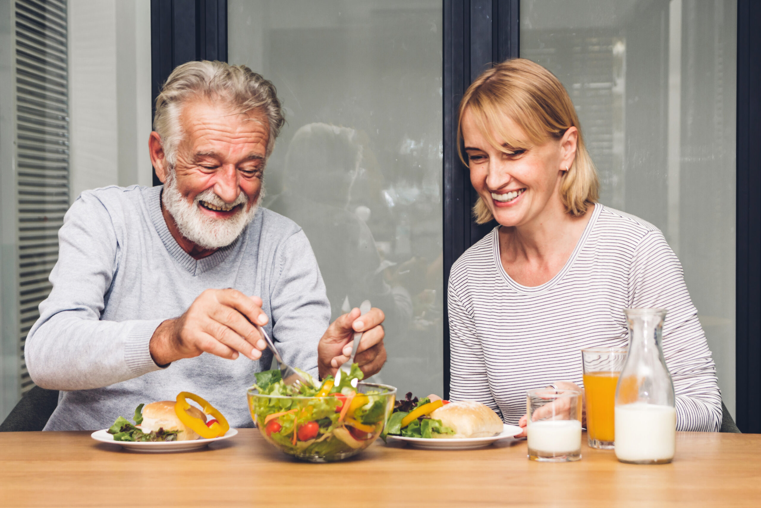 Two smiling senior adults share a healthy meal at a table.