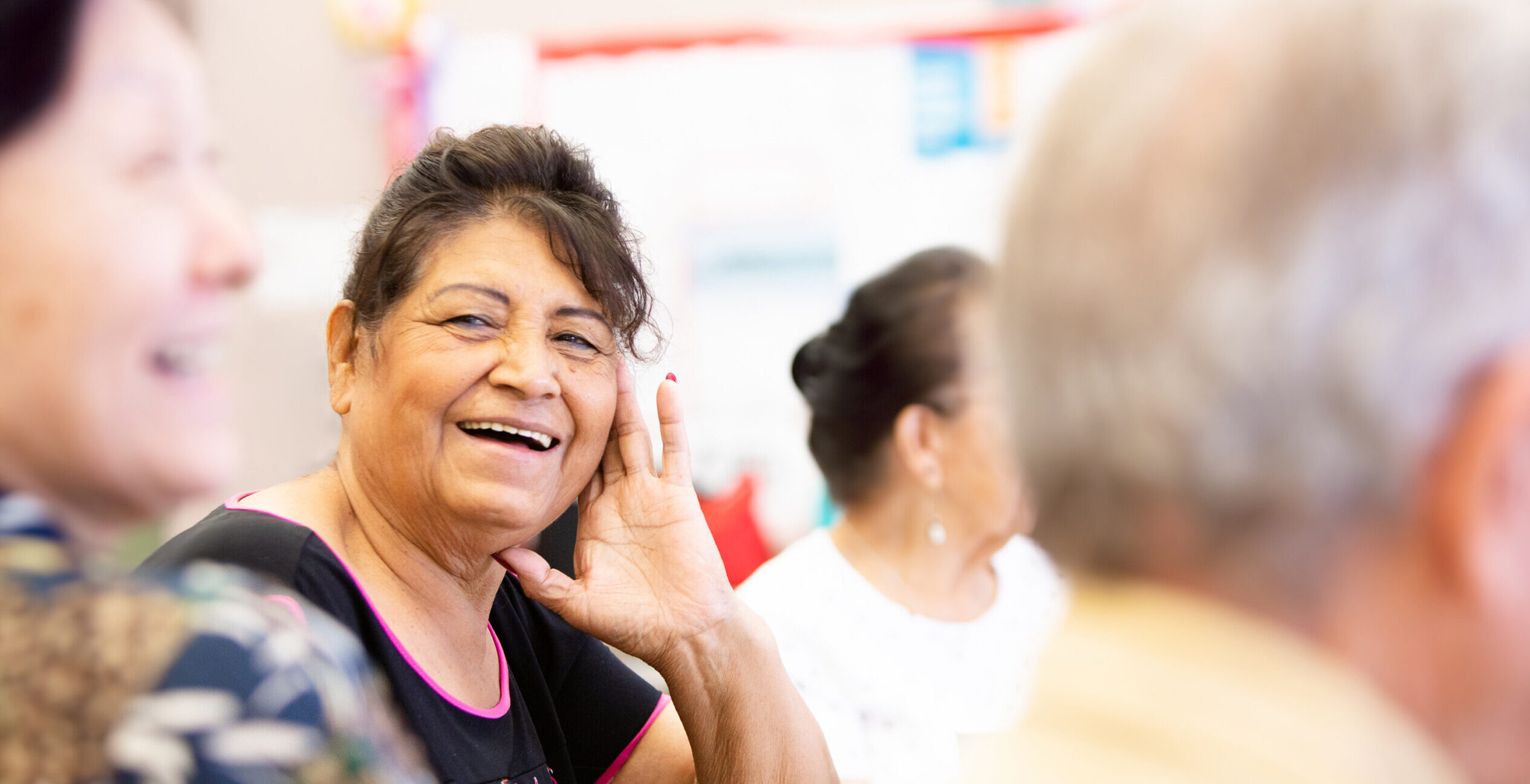 A smiling senior woman at a table with other adults.
