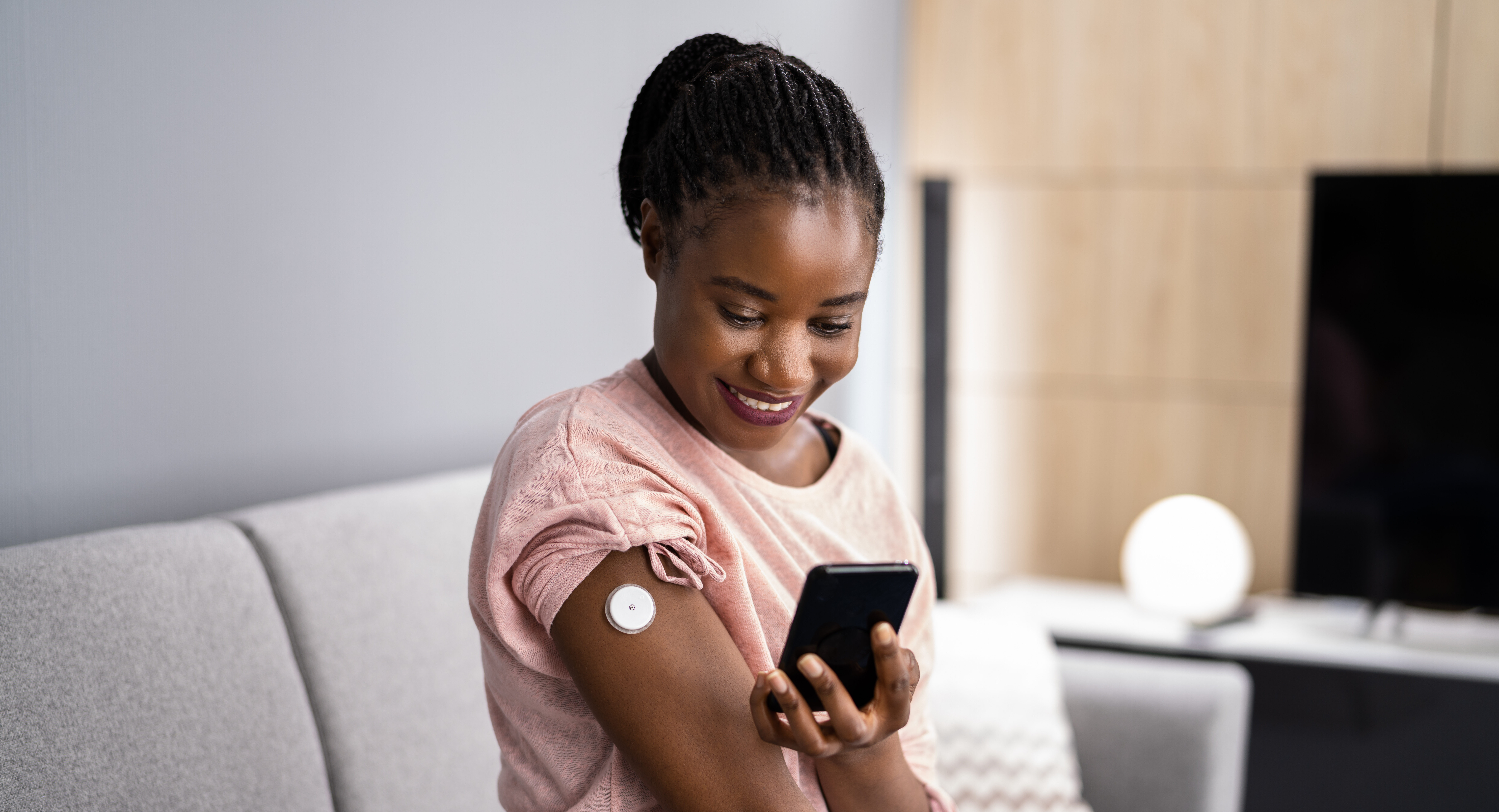 Smiling woman checks continuous glucose monitor sensor on arm with smartphone.